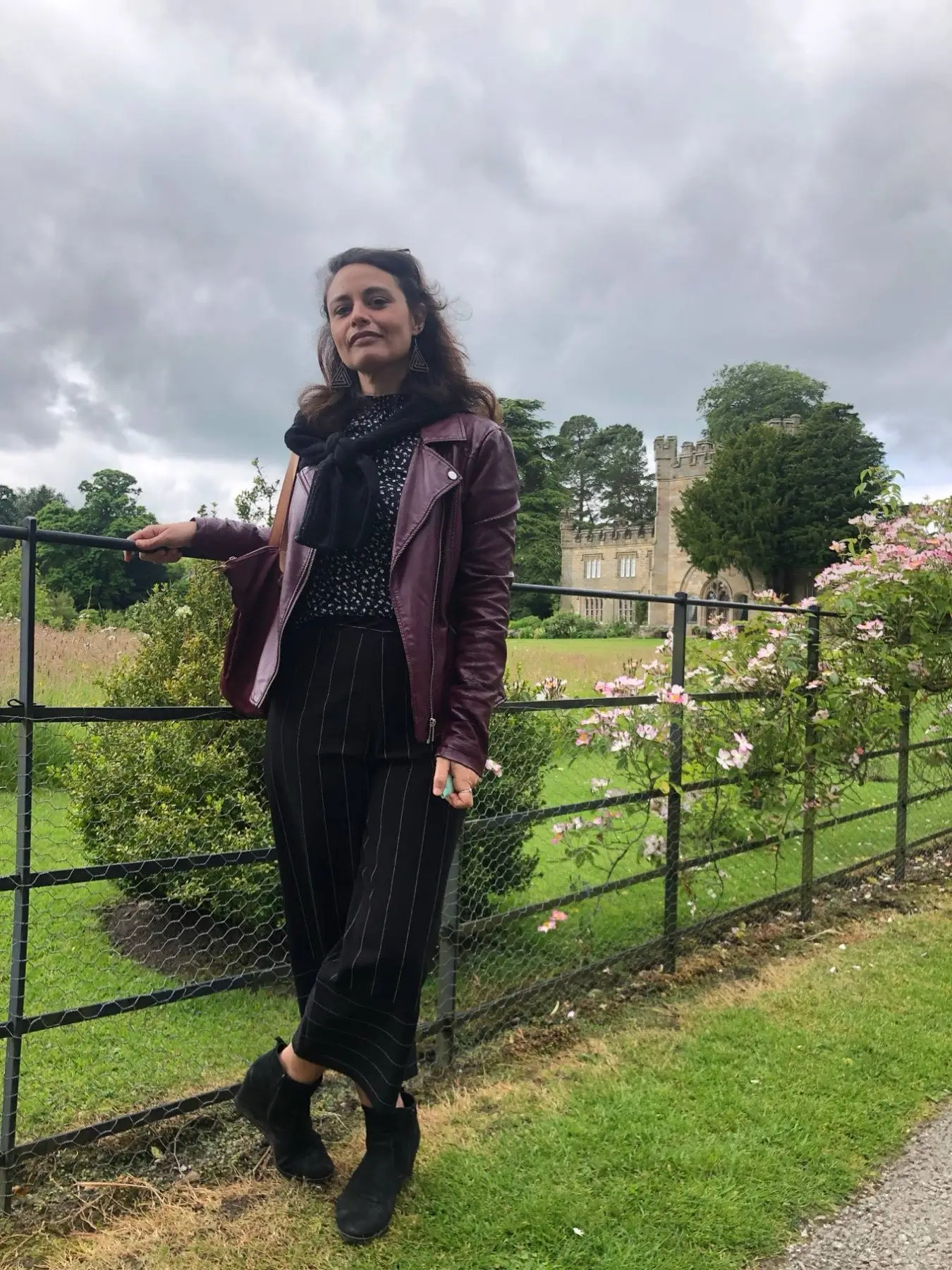 Ines in a burgundy leather jacket leaning on a garden railing