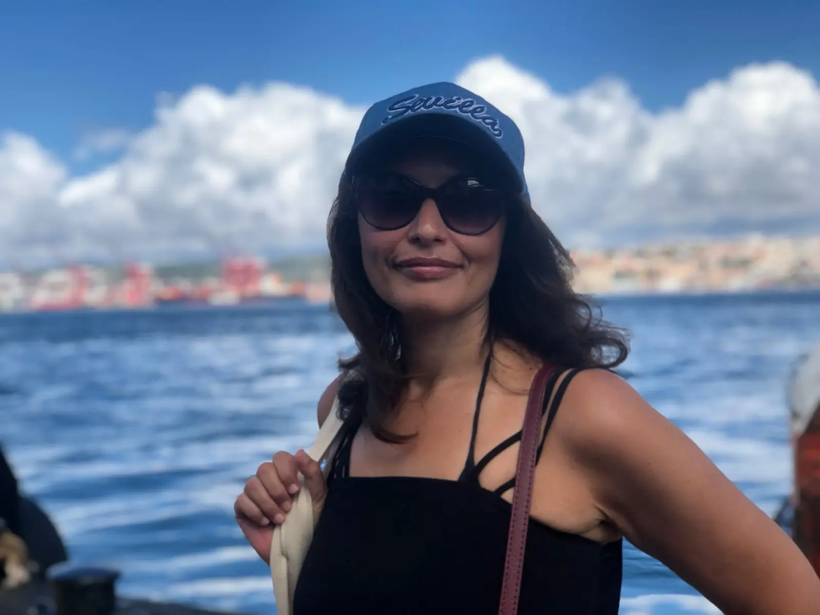 Ines in a cap and sunglasses by the water on a bright day